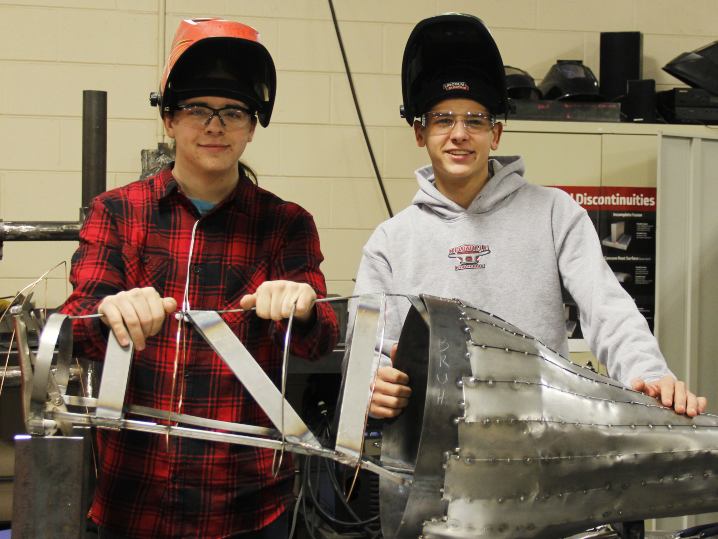 two students next to welding sculpture